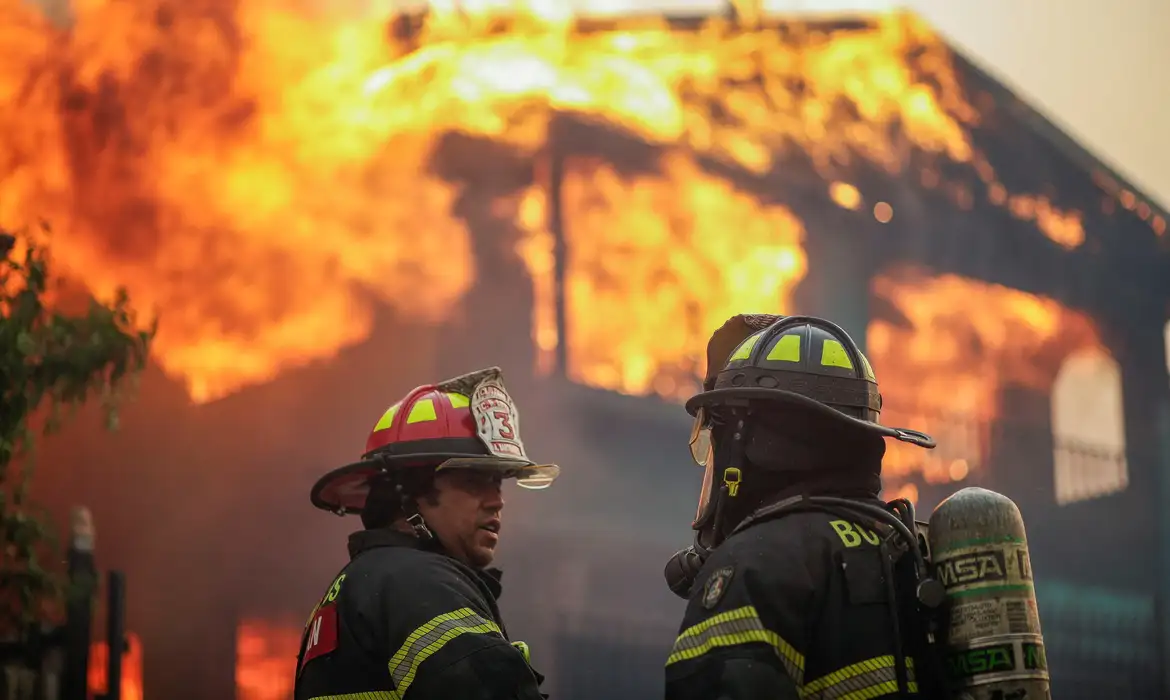 Firefighters stand in front of a burning building in the aftermath of a forest fire in the Biobio region where, according to local media, multiple wildfires prompted emergency evacuations, in Concepcion, Chile, January 18, 2026. REUTERS/Juan Gonzalez
