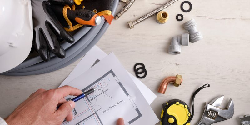 imagem de itens de reforma e obra em uma mesa com as maos de um homem segurança um projeto impresso