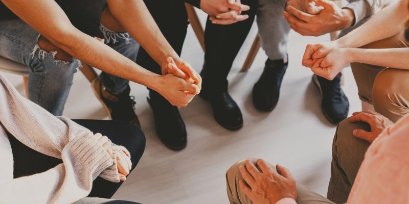 imagem mostrando apenas maos e pernas de varios homens sentados em circulo