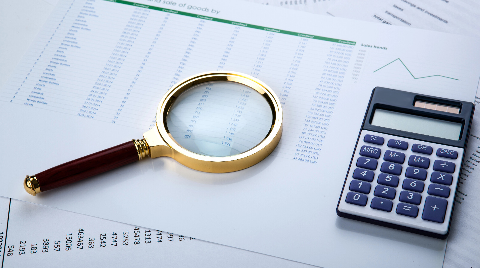 lupa sobre papel com numeros e uma calculadora do lado indicando movimentacao financeira