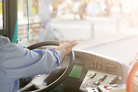 Imagem mostra motorista de onibus segurando o volante e ao fundo a rua embaçada