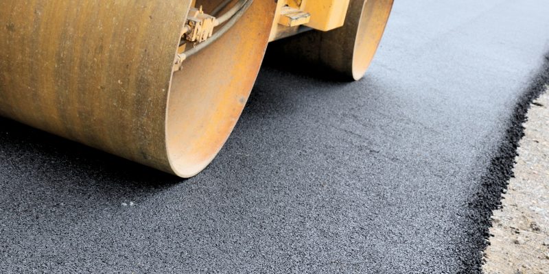 rolo compressor de metal amarelo compacta uma camada de asfalto preto e fresco em uma estrada em construção.