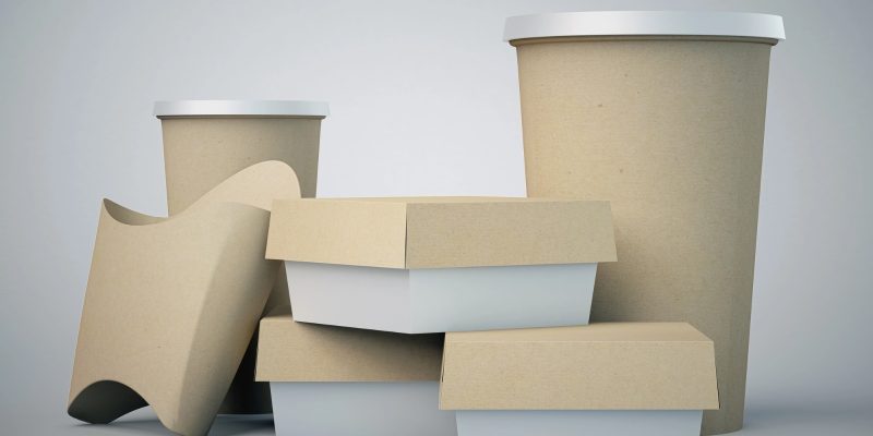 Uma seleção de embalagens para fast-food em papel kraft e branco, incluindo copos com tampa, caixas de hambúrguer e um porta-batatas, dispostos sobre um fundo cinza claro.