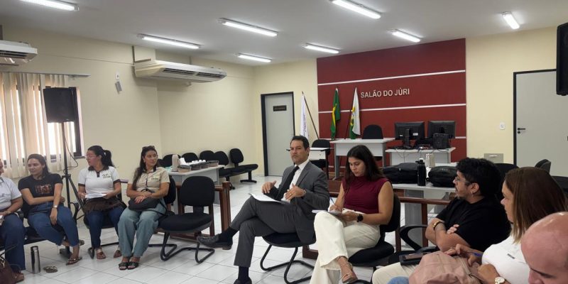 Pessoas sentadas em círculo participando de uma reunião em uma sala com a inscrição 