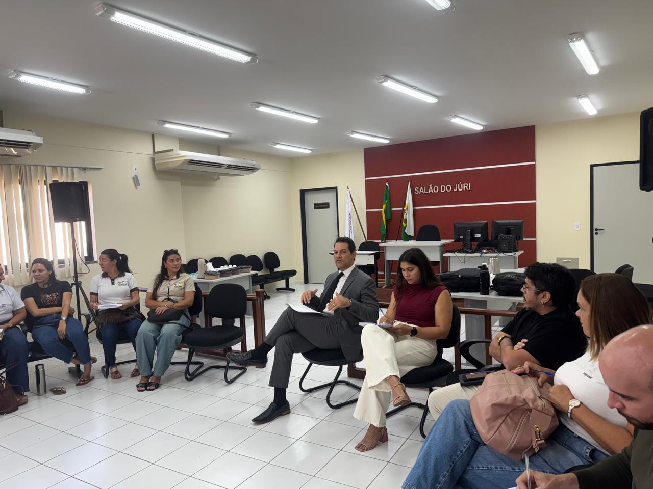Pessoas sentadas em círculo participando de uma reunião em uma sala com a inscrição 