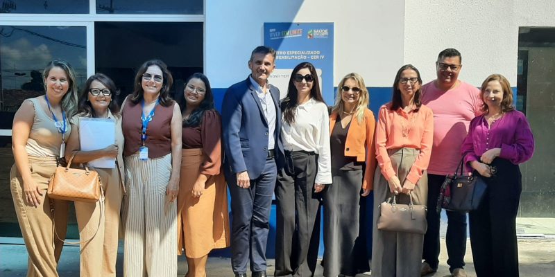 grupo de dez pessoas, vestidas com trajes casuais e formais, sorrindo e posadas lado a lado em frente à entrada de um prédio público