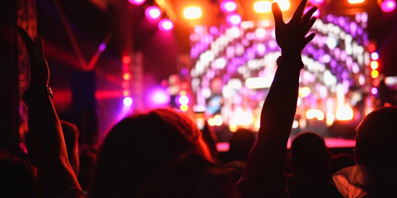 imagem de pessoa com as maos pra cima em uma festa com o palco ao fundo