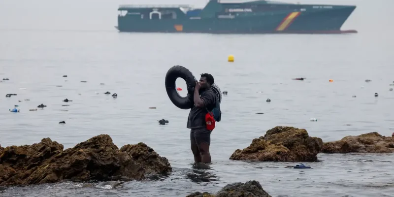 A man holds an inflatable ring, as he stands in the water, with the Spanish Guardia Civil (Civil Guard) in the background, amid mass crossings of migrants on foot and by sea from Morocco into Spanish territory, in Ceuta, Spain, July 31, 2026. REUTERS/Jon Nazca        TPX IMAGES OF THE DAY