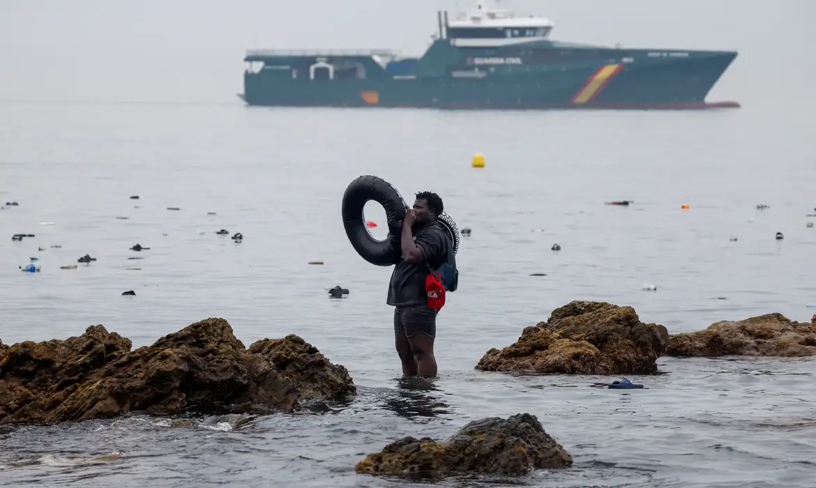 A man holds an inflatable ring, as he stands in the water, with the Spanish Guardia Civil (Civil Guard) in the background, amid mass crossings of migrants on foot and by sea from Morocco into Spanish territory, in Ceuta, Spain, July 31, 2026. REUTERS/Jon Nazca        TPX IMAGES OF THE DAY