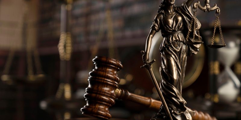 Martelo de madeira da Justiça perto de uma estatua de bronze da Justiça em tamanho pequeno.