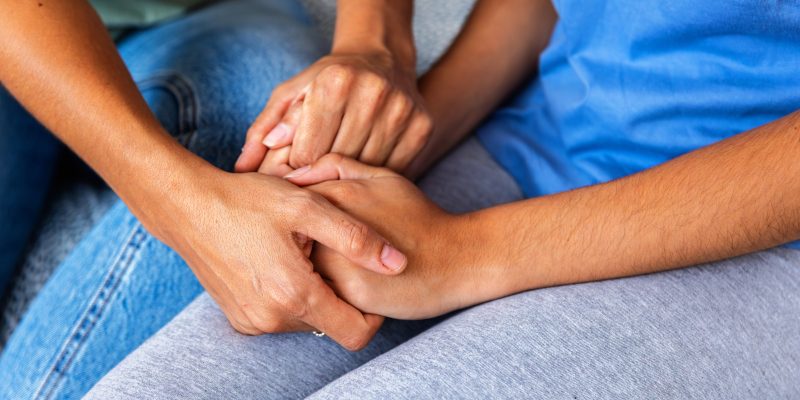 Plano próximo das mãos de duas pessoas unidas em um gesto de carinho, apoio e empatia.