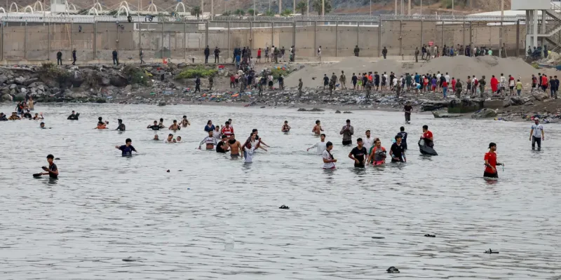 People waddle through water to enter Spain, and in the background people who just entered Spain return back to Morocco, amid mass crossings of migrants on foot and by sea from Morocco into Spanish territory, in Ceuta, Spain, July 31, 2026. REUTERS/Jon Nazca  REFILE - CHANGES SLUG