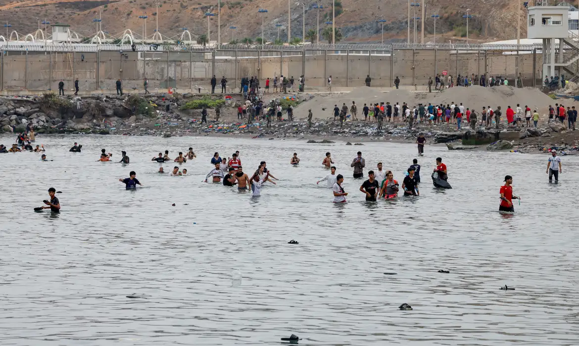 People waddle through water to enter Spain, and in the background people who just entered Spain return back to Morocco, amid mass crossings of migrants on foot and by sea from Morocco into Spanish territory, in Ceuta, Spain, July 31, 2026. REUTERS/Jon Nazca  REFILE - CHANGES SLUG