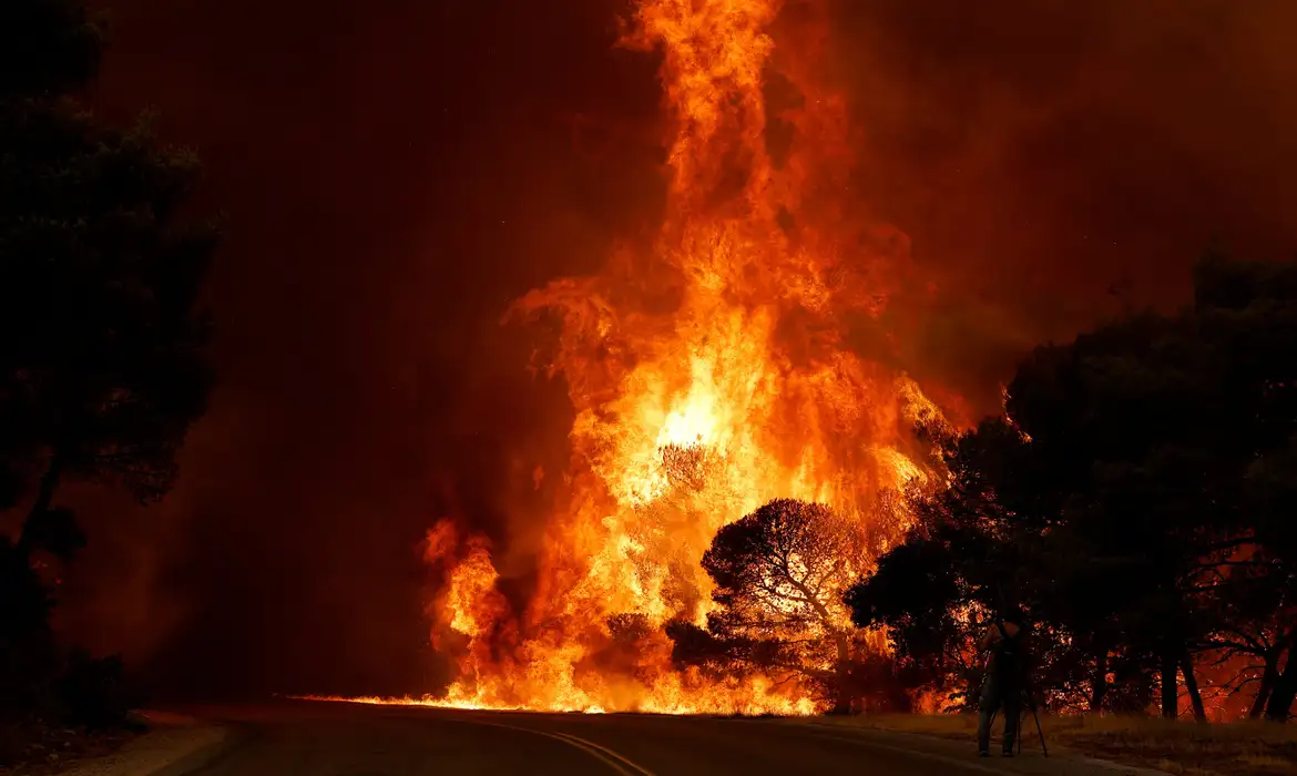Um homem grava imagens enquanto a fumaça e as chamas se elevam de um incêndio florestal próximo a Agia Paraskevi, na Grécia, em 1º de agosto de 2026. REUTERS/Louisa Gouliamaki/Proibida Reprodução