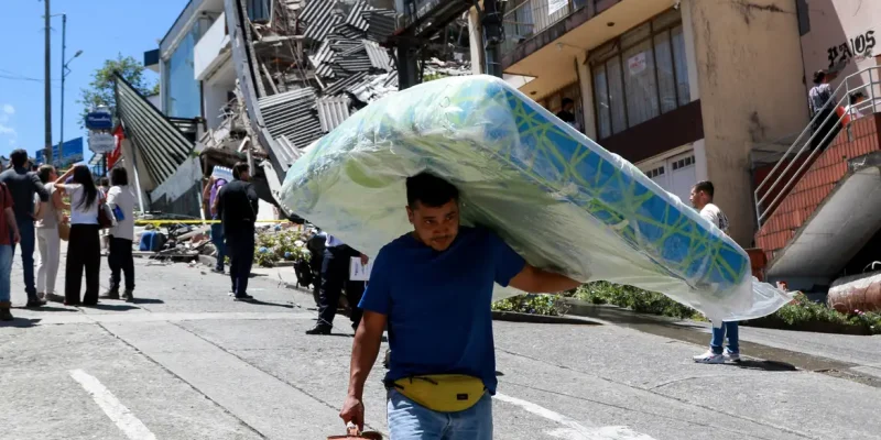 A man carries a mattress down the street in front of damaged buildings after an earthquake, in Manizales, Colombia August 10, 2026. REUTERS/Andres Camilo Valencia/Proibida Reprodução