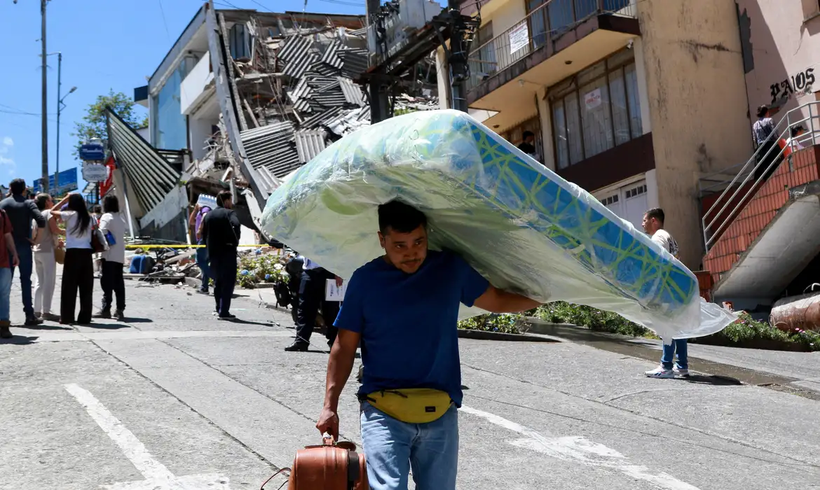 A man carries a mattress down the street in front of damaged buildings after an earthquake, in Manizales, Colombia August 10, 2026. REUTERS/Andres Camilo Valencia/Proibida Reprodução