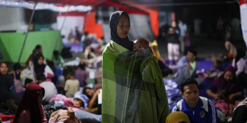 A woman holds a baby as people rest in a shelter at a makeshift evacuation center at a stadium in the aftermath of an earthquake, in Maumere, East Nusa Tenggara, Indonesia, August 16, 2026.  REUTERS/Edgar Su/Proibido Reprodução
