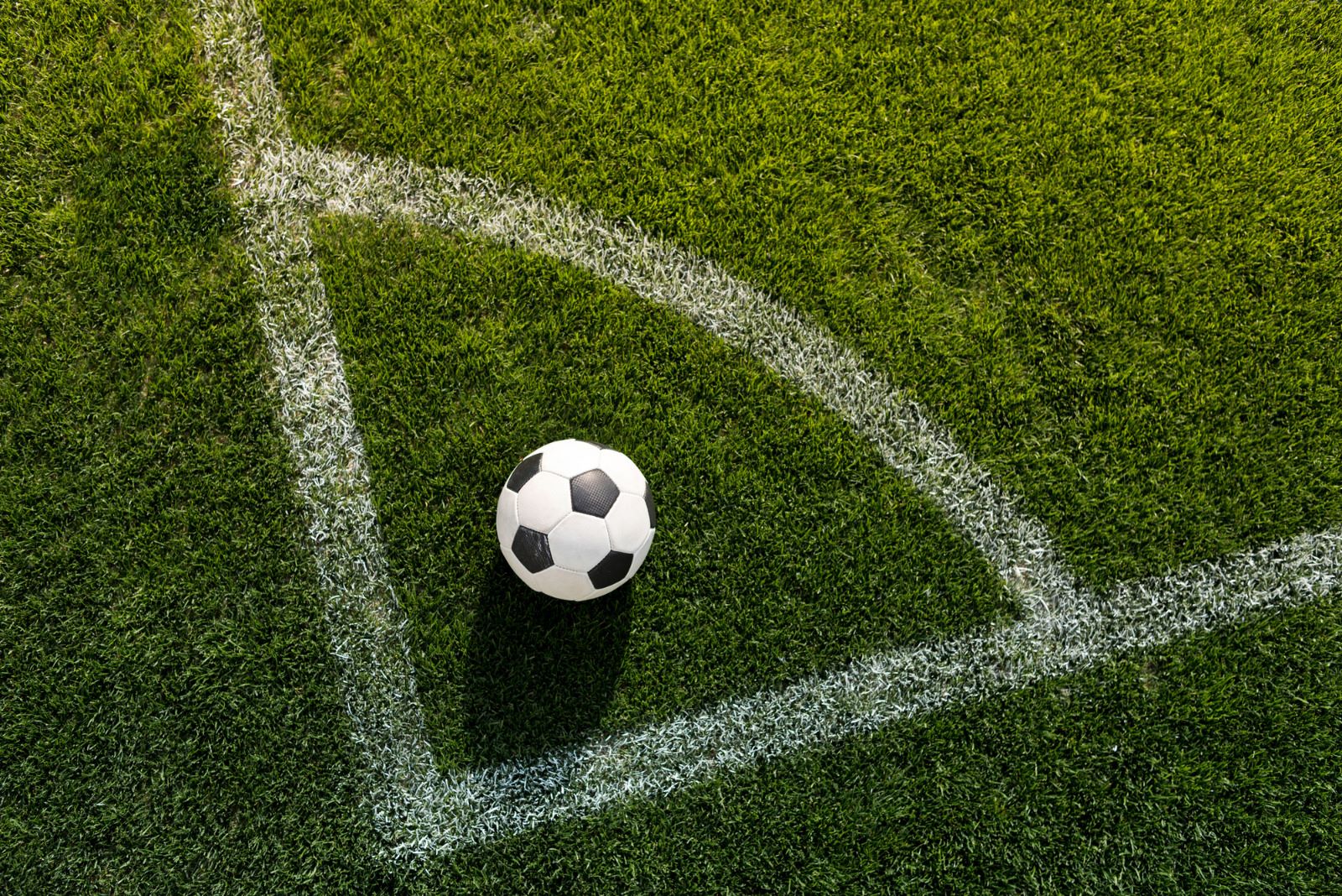 bola de futebol sobre gramado verde posicionada exatamente no local de bater escanteio