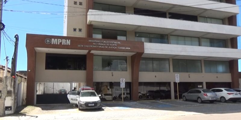 Fachada do prédio do Ministério Público do Rio Grande do Norte (MPRN), na sede das Promotorias de Justiça de Candelária, com carros estacionados à frente, incluindo uma viatura da polícia.