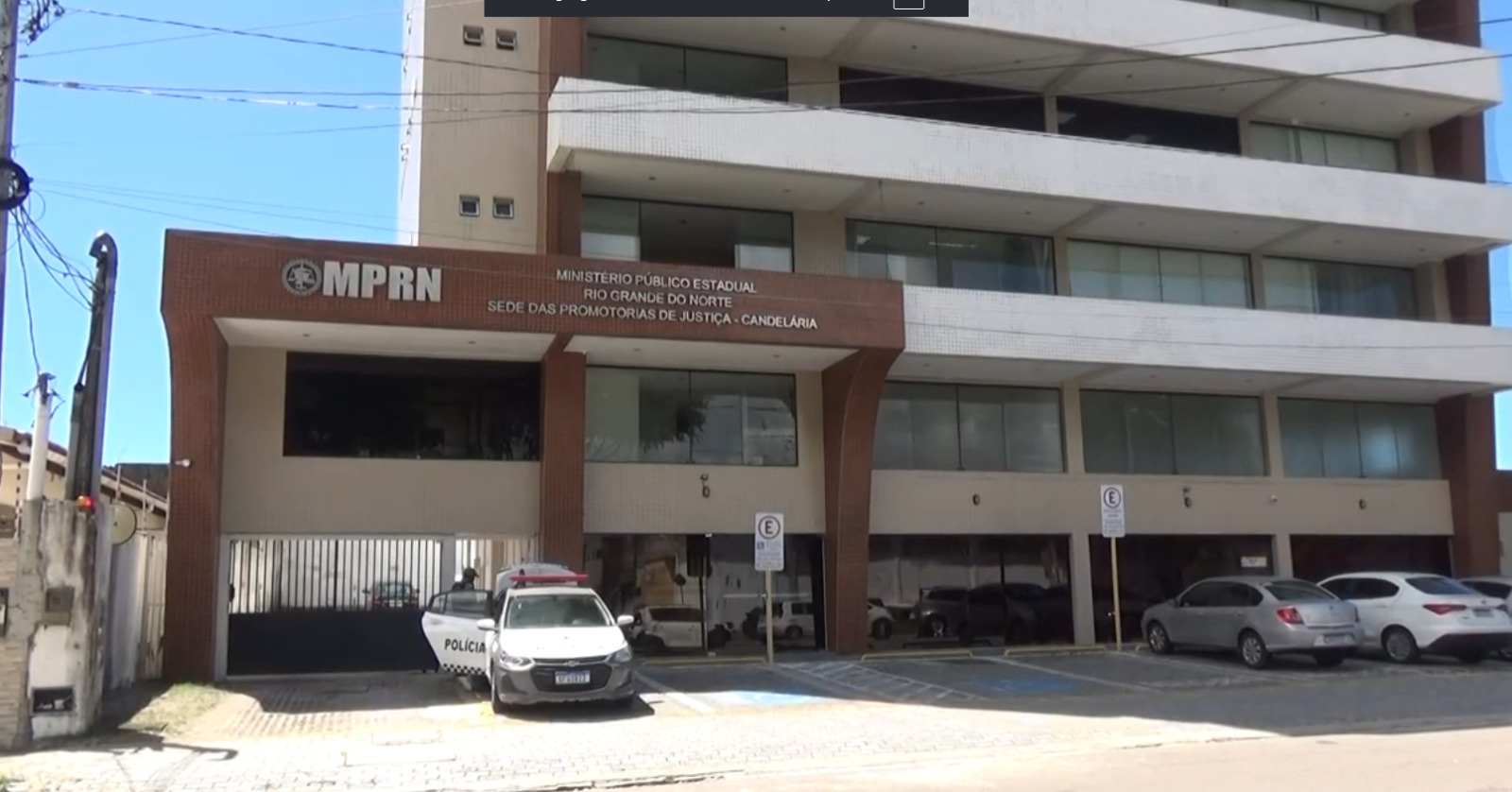 Fachada do prédio do Ministério Público do Rio Grande do Norte (MPRN), na sede das Promotorias de Justiça de Candelária, com carros estacionados à frente, incluindo uma viatura da polícia.