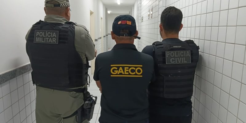 três homens de costas, sendo dois deles com farda da PM e um com uniforme e bone do gaeco/mprn